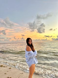 a woman standing on top of a sandy beach next to the ocean with her hands in her pockets