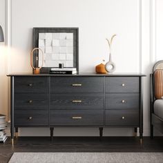 a black dresser with gold handles in a white room next to a bed and lamp