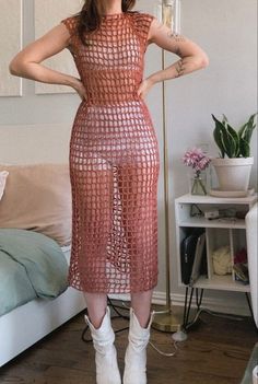 a woman standing in front of a bed wearing white boots and a red mesh dress