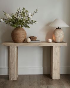 a wooden table with two vases and a lamp on it next to a wall