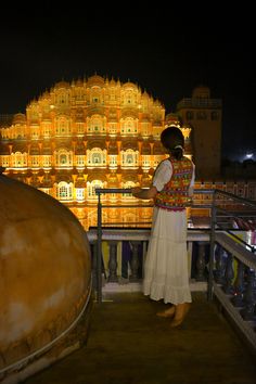 a woman standing on top of a balcony next to a giant golden building at night