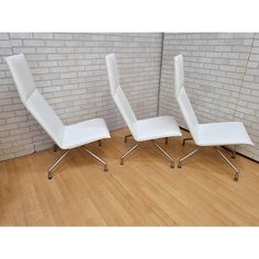 two white chairs sitting next to each other on a hard wood floor in front of a brick wall