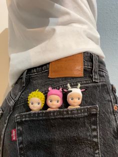 two small dolls are in the back pocket of someone's jean pants, with their backs to the camera