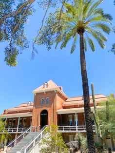 a tall palm tree sitting in front of a red brick building with stairs leading up to it