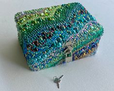 a small beaded box with a key on the side and a chain attached to it