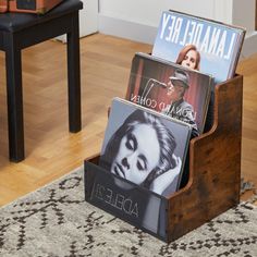 a wooden magazine holder with magazines in it on the floor next to a rug and chair