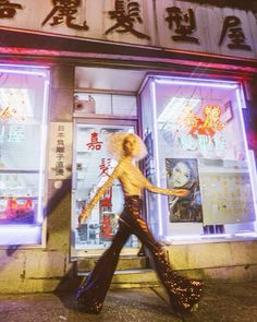 a woman is walking down the street in front of a store with neon lights on it