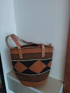 Geometrical earth tone sisal tote bag. Unique and stylish colorful sisal kiondo bag with stitched leather straps, pocket lining and zipper. Patterns and sizes slightly vary because weaving and stiching is done by hand. Ideal as a beach bag, shopping basket, market basket or storage basket. This unique tote bag is handmade by a group of ladies in a remote rural village in Machakos, Kenya. Do not clean with brush or water. If the bag gets wet, please dry to avoid dampness.  Leather type used is bo Market Tote Shoulder Bag With Leather Handles, Tote Shoulder Bag With Leather Handles For Market, Leather Handle Tote Shoulder Bag For Market, Handheld Bags With Leather Handles For Shopping, Handheld Shopping Bag With Leather Handles, Square Handwoven Bucket Bag For Travel, Rectangular Bucket Bag With Leather Handles For Market, Handwoven Shoulder Bag With Double Handle For Daily Use, Rectangular Brown Bucket Bag For Shopping