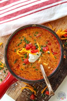 a bowl of chili cheese soup on a cutting board with a red handled utensil