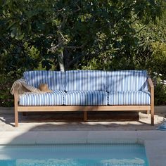 a blue and white striped couch next to a swimming pool with trees in the background