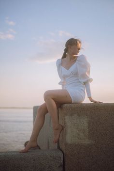 a woman sitting on top of a stone wall next to the ocean