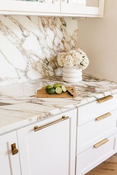 a marble counter top in a kitchen with white cabinets and gold pulls on the handles