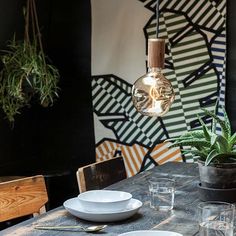 a table with plates and cups on it in front of a wall with plants hanging from it