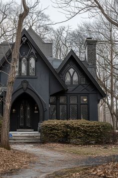 a black house in the middle of a leafy area with trees and bushes around it