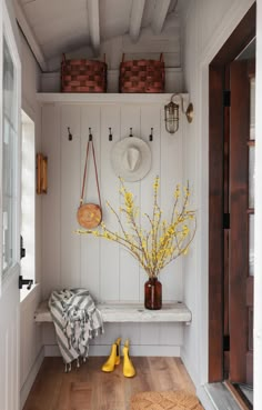 a white bench with yellow flowers and baskets on it next to a wooden table in front of a door