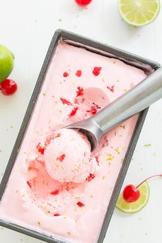 a scoop of ice cream in a pan with limes and cherries around it