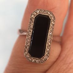 a close up of a person's hand holding a ring with an oval shaped black stone