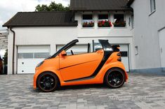 an orange smart car parked in front of a house