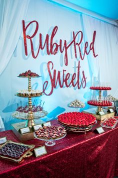 a red table topped with lots of desserts next to a sign that says rubyfred sweets