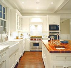 a kitchen with white cabinets and wood counter tops, along with a stainless steel stove top oven