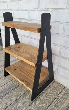 a wooden shelf sitting on top of a wooden floor next to a brick wall with black metal legs