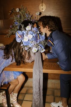 two people sitting at a table with flowers in front of their faces, one kissing the other