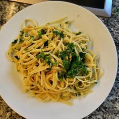 a white plate topped with pasta and broccoli on top of a granite counter