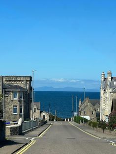 an empty street next to the ocean with houses on both sides and mountains in the distance