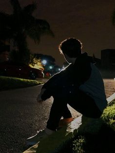 a person sitting on the side of a road at night with their back to the camera