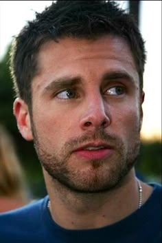 a close up of a person wearing a blue shirt and looking at the camera with a serious look on his face