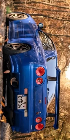 a blue car parked next to a tree with its hood up on it's trunk