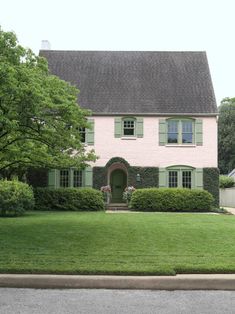 a pink house with green shutters on the front and lawn in front of it