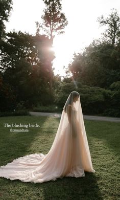 a woman in a wedding dress standing on the grass with her back to the camera