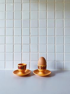 two yellow cups and saucers sitting on a white counter next to a tiled wall