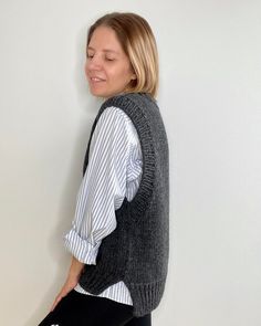 a woman in black leggings standing next to a white wall wearing a gray vest and striped shirt