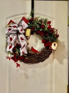 a christmas wreath hanging on a door with red and white bows, bells and holly