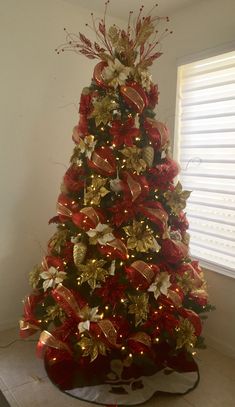 a red and gold christmas tree decorated with bows, poinsettis and ribbons