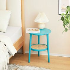 a small blue table with a white lamp on it next to a bed and a potted plant