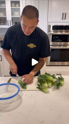 a man cutting green onions on top of a kitchen counter