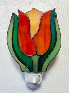 a stained glass flower is mounted on a white light switch cover with an orange, green and red design