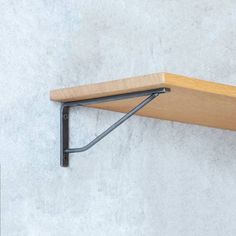 a wooden shelf with black metal brackets on it's sides against a white wall