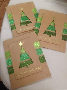 three brown christmas cards with green glitter trees on them, sitting on a white table