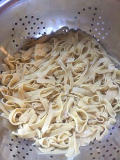 a bowl filled with pasta sitting on top of a metal tablecloth covered floor next to a colander