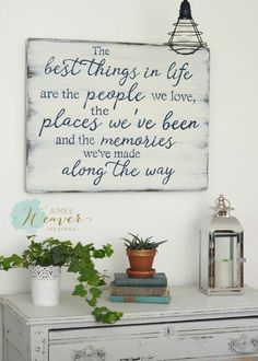 a white dresser topped with books and plants next to a wall mounted sign that says the best things in life are the people we love