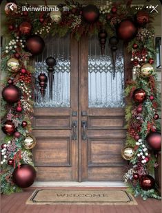 two wooden doors decorated with christmas ornaments and greenery for the holiday season in front of them