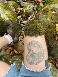 a person with a tattoo on their leg next to some rocks and leaves in the woods