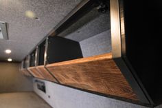 the inside of a motor home with wood and metal shelves on the wall, along with recessed lighting