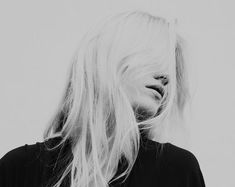 black and white photograph of woman with long blonde hair looking to the side in front of grey background