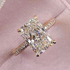 an engagement ring with a princess cut diamond surrounded by pave diamonds on pink velvet