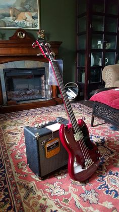 a red guitar sitting on top of a rug in front of a fire place with an amp